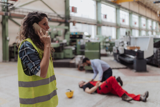 Woman is calling ambulance for her colleague after accident in factory. First aid support on workplace concept.