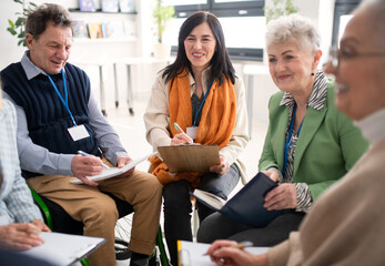 Excited elderly people attending group therapy session at nursing house, positive senior man and woman sitting in circle, having conversation with psychologist - obrazy, fototapety, plakaty