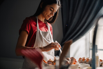 Young hispanic woman using tablet-computer while cooking in kitchen
