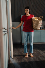 Young woman holding basket with clothes while doing laundry at home