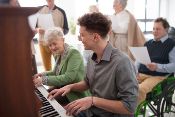 Senior woman with young teacher playing at piano in choir rehearsal. - obrazy, fototapety, plakaty