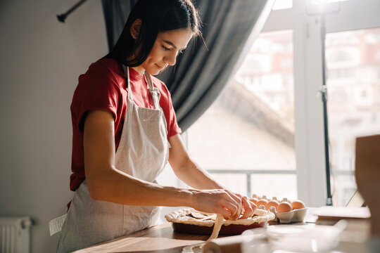 Young hispanic woman wearing apron making pie in kitchen at home