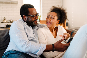 African american woman and man smiling and using cellphone at home