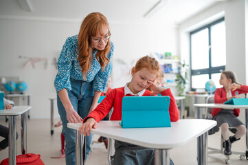Schoolgirl using tablet with help of teacher during class at school.