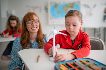 Down syndrome schoolgirl with model of wind turbine with help of teacher learning about...