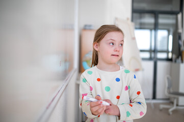 Little schoolgirl with down syndrome standing in front of whiteboard