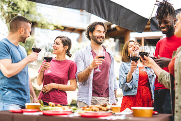 Group of happy friends having fun while drinking red wine and eating food at party, focus on young bearded handsome man, genuine people