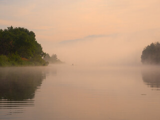 fog over the river at sunset a fisherman in a boat on the water