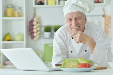 Portrait of elderly male chef cooking at table with laptop