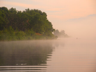 fog over the river at sunset a fisherman in a boat on the water
