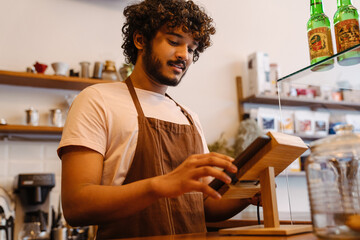 Young indian handsome curly barista working with tablet