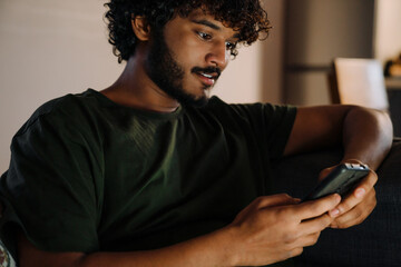 Young handsome indian man using his phone sitting on sofa