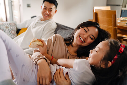 Happy asian family with little girl laughing while sitting on sofa
