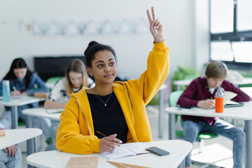 High school students paying attention in class, sitting in their desks and raising hand.