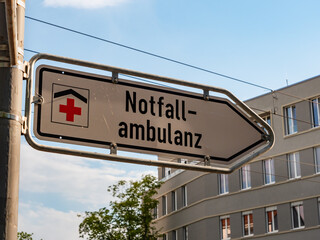 Notfallambulanz sign in Germany (emergency department). Signpost guiding to the entrance of a hospital. Urgent health treatment for accident victims. Sunset light is shining on the metal plate.