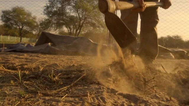 man digging dry land with a shovel at sunset in slow motion