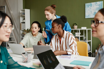 Group of female colleagues using laptop working over new project at table during teamwork at office
