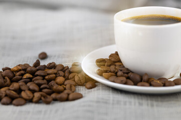 A cup of coffee and coffee beans on a burlap cloth.