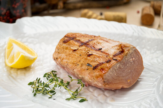 grilled fish fillet on a white plate with lemon and thyme sprig, macro photo
