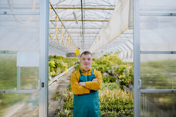 Young employee with Down syndrome working in garden centre, looking at camera and standing in door...