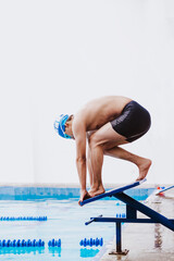 latin teenager man swimmer athlete wearing cap and goggles in a swimming training holding On...