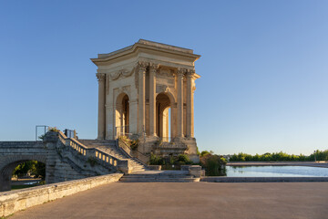 Fototapeta na wymiar Scenic summer morning side view of the historic ancient water tower stone building and water pool in landmark Promenade du Peyrou garden, Montpellier, France