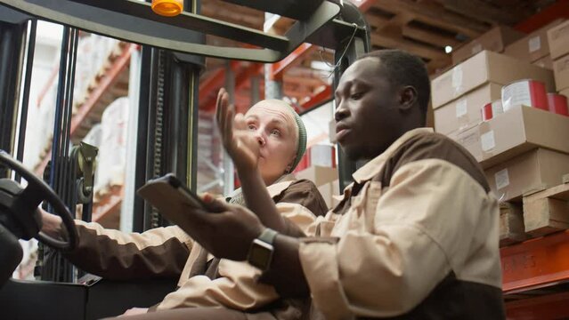 African American manager using digital tablet and giving instructions to Caucasian female forklift operator while working together in warehouse