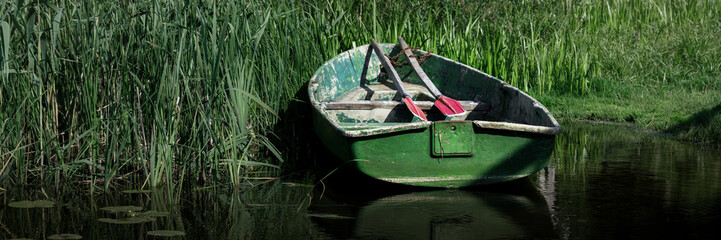 Vintage wooden boat with oars is moored on riberbank. Fishing concept.