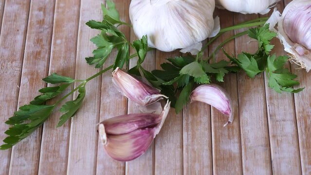 Cutting board with fresh seasonings on a wooden background. White garlic heads and cloves and parsley leaves. Condiments 