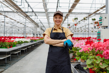 Cheerful female flowers greenhouse worker holding protective gloves in her hands