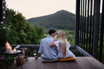 Young couple in love resting outdoors on terrace of tiny house in woods with view in evening,...
