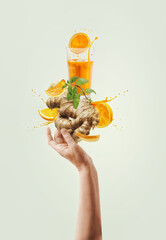 Women hand holding balancing ginger and orange immunity boosting drink with splashing and...