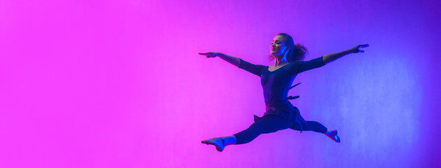 Modern dance girl dancer jumping up dancing in neon light doing gymnastic exercises in studio, wide banner, copy space.