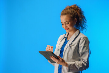 Studio shot of a young female doctor using a digital tablet against a blue background.