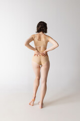Back view of young beautiful slim girl in underwear posing isolated over gray studio background. Wellness, wellbeing, fitness, fashion concept.