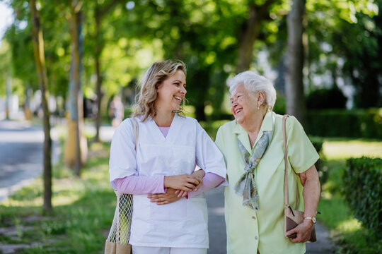 Portrait of caregiver with senior woman on walk in park with shopping bag, looking at caemra.