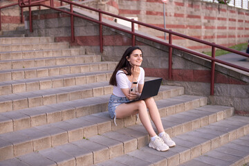 the girl is sitting on the stairs, laptop on her lap, looking into the distance