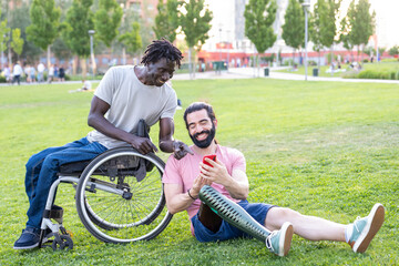 two friends with disability chatting and using smartphone outdoor, people using modern device to...