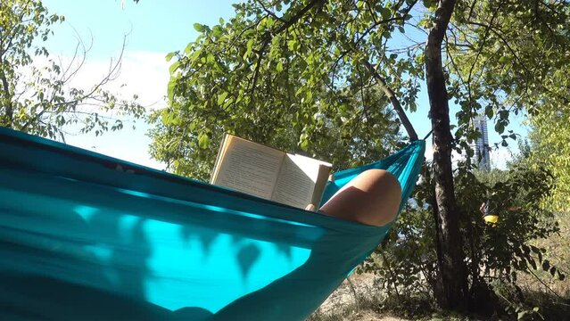 4K view of a man reading a book in a hammock in a summer garden.