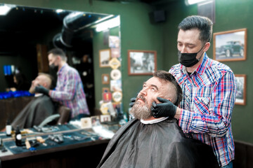 Barber gives a beard massage to an older man in a barbershop.