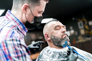 Beard dyeing in a barbershop. a young master applies paint An adult man in a barbershop with a beard and a mohawk.