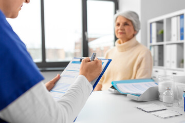 medicine, health and vaccination concept - close up of doctor with clipboard and senior woman at hospital