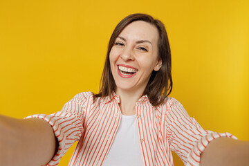 Close up young happy smiling cheerful woman she 30s wears striped shirt white t-shirt doing selfie shot pov on mobile cell phone isolated on plain yellow background studio. People lifestyle concept.