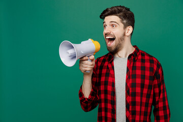 Young happy smiling man he 20s in red shirt grey t-shirt hold scream in megaphone announces discounts sale Hurry up isolated on plain dark green background studio portrait. People lifestyle concept.