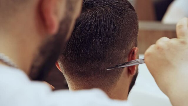 Barber doing a haircut to male client in barbershop close up