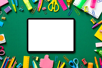 Digital tablet mockup with colorful school stationery on green table. Back to school, e-earning, online lessons concept.