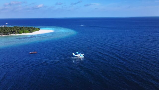Seaplane takes off in the Indian Ocean with Tropical Maldivian island on the background. Coral reef and turquoise sea water. Vakkaru, Maldives.