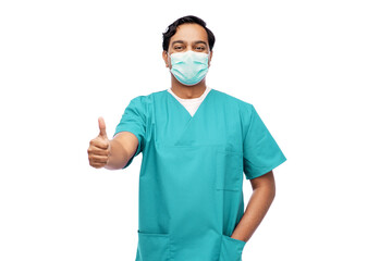 healthcare, profession and medicine concept - indian doctor or male nurse in blue uniform and face protective medical mask for protection from virus disease showing thumbs up over white background