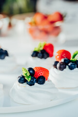 Meringue dessert Pavlova cake with fresh cream, strawberries and blueberries, decorated with mint on the white plate. Recipes for delicious light desserts. Confectionery cafe menu. Selective focus