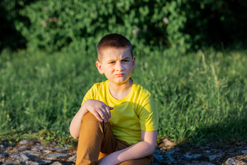 schoolboy boy in a yellow T-shirt sits outdoors